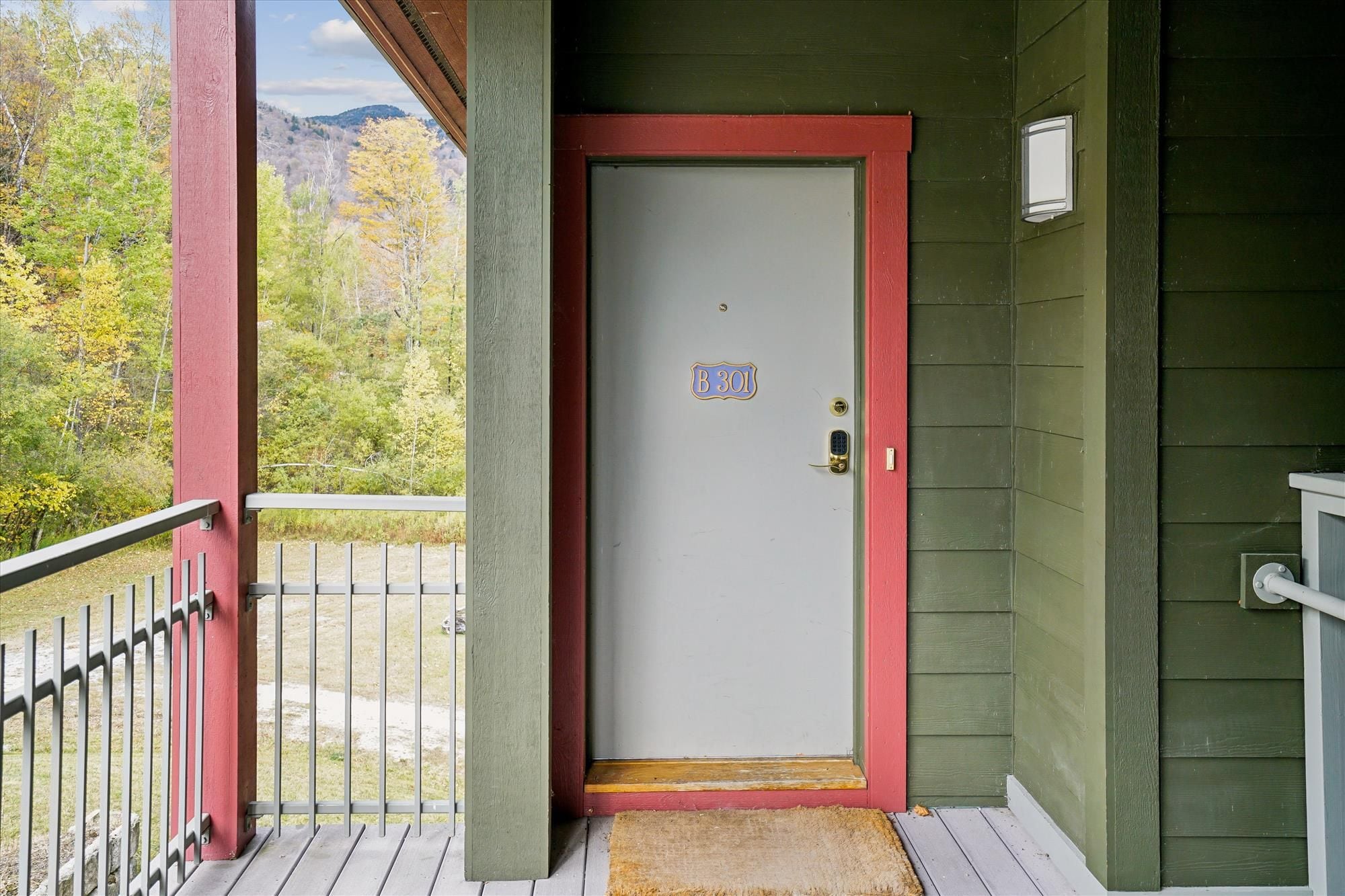 A house with a white door and a red frame, a mailbox, and a view of trees and mountains.