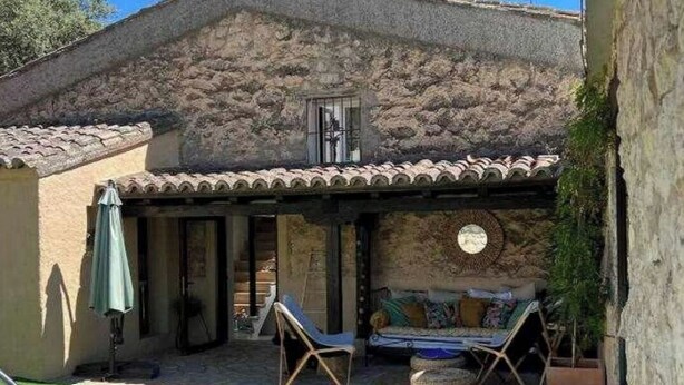 Un bâtiment en pierre avec un toit en tuiles, une piscine et un espace extérieur aménagé pour s’asseoir.