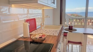 Une cuisine moderne avec vue sur la mer, dotée d’un plan de travail en bois, d’un étendoir rouge et d’un panier contenant des torchons.
