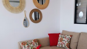 Un salon avec un canapé beige, deux coussins rouges, un coussin à motifs floraux et un vase contenant des tulipes rouges. On peut voir trois miroirs de styles différents accrochés au mur.