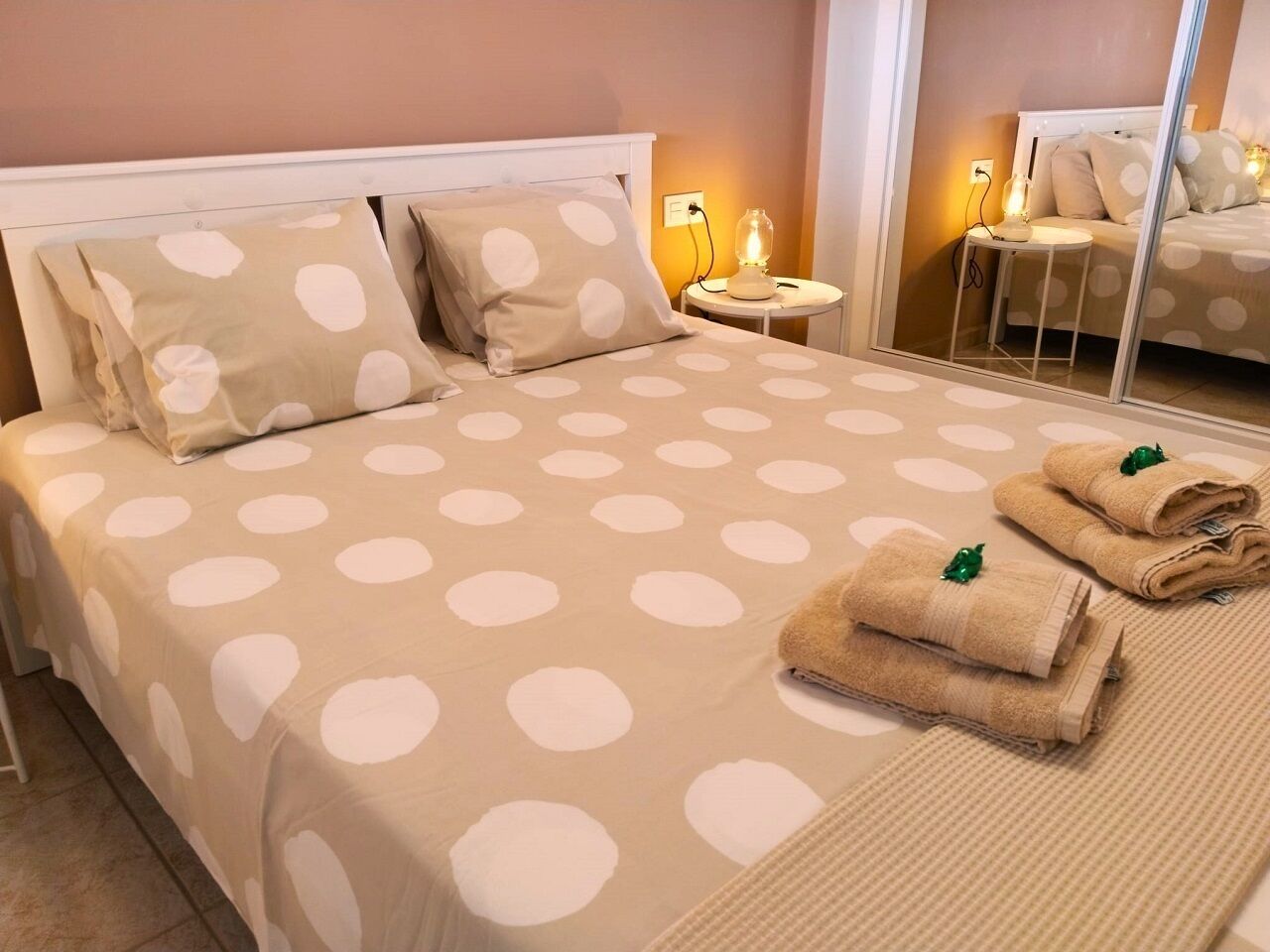 Un lit bien fait, recouvert d’une couvre-lit à pois, avec deux oreillers et deux serviettes pliées décorées d’un motif de feuille verte.