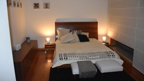 Une chambre à coucher bien aménagée, avec une tête de lit en bois, un grand lit recouvert d’une literie à motifs, des lampes de chevet et une petite table de chevet avec une lampe.