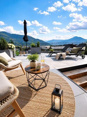 Une terrasse sur le toit avec des sièges extérieurs, une table avec des boissons et une vue sur les montagnes.