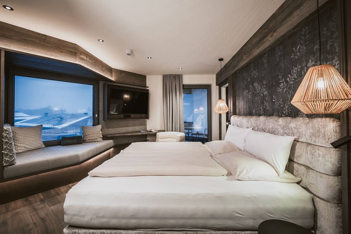 Ein modernes Hotelzimmer mit einem großen Bett, einem Fernseher, Blick auf eine Stadtlandschaft und einem Balkon.
