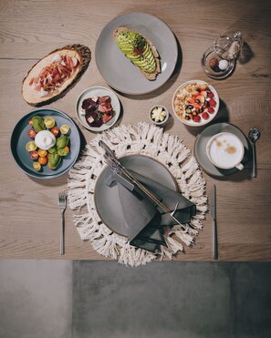 Une table dressée avec différents plats, notamment une assiette de jambon cru, un saladier, une tasse de café et un centre de table décoratif.