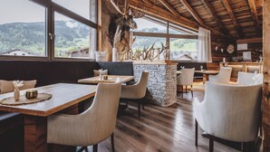L’intérieur est rustique, avec des poutres en bois, une cheminée en pierre et une grande tête de cerf accrochée au mur. Des tables et des chaises sont disposées pour les repas.