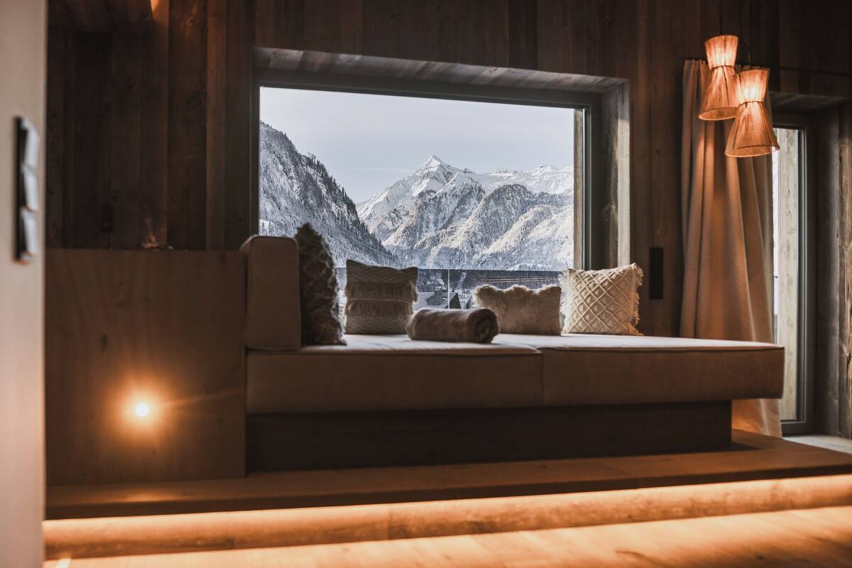 Eine gemütliche Sitzecke mit Blick auf schneebedeckte Berge durch ein großes Fenster.