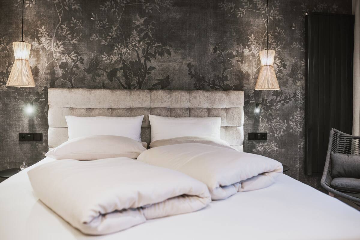 Ein modernes Schlafzimmer mit einem großen Bett, zwei Wandlampen und floralem, dunkel gestreiftem Wandpapier.