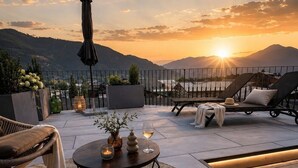 Une terrasse sur le toit offrant une vue sur le coucher de soleil, des chaises longues, une table ronde avec des bougies et une lanterne.