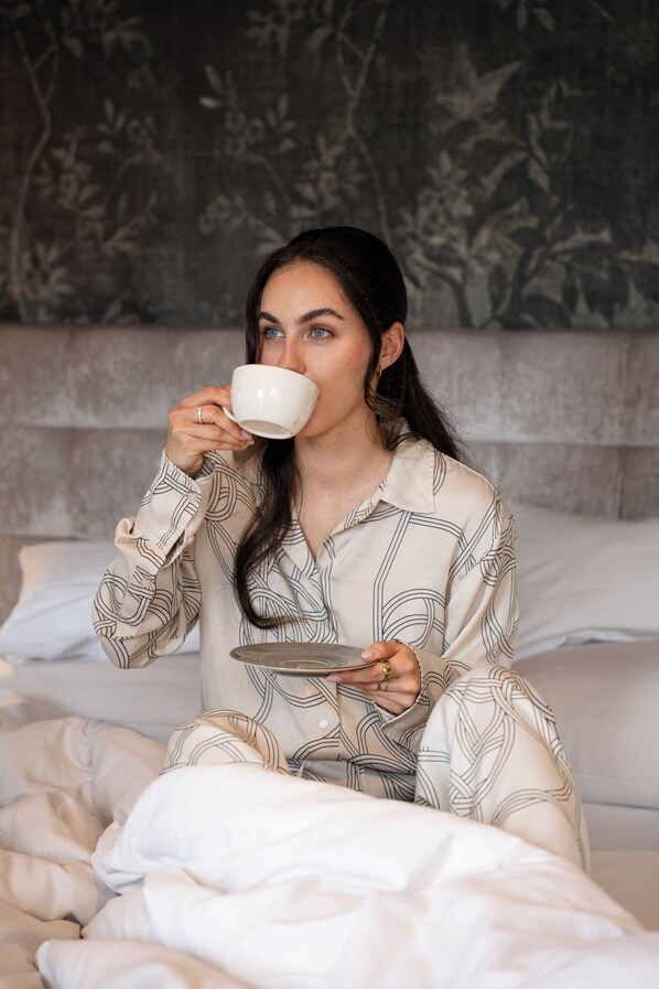 A person sitting on a bed with a cup in hand, holding a plate.