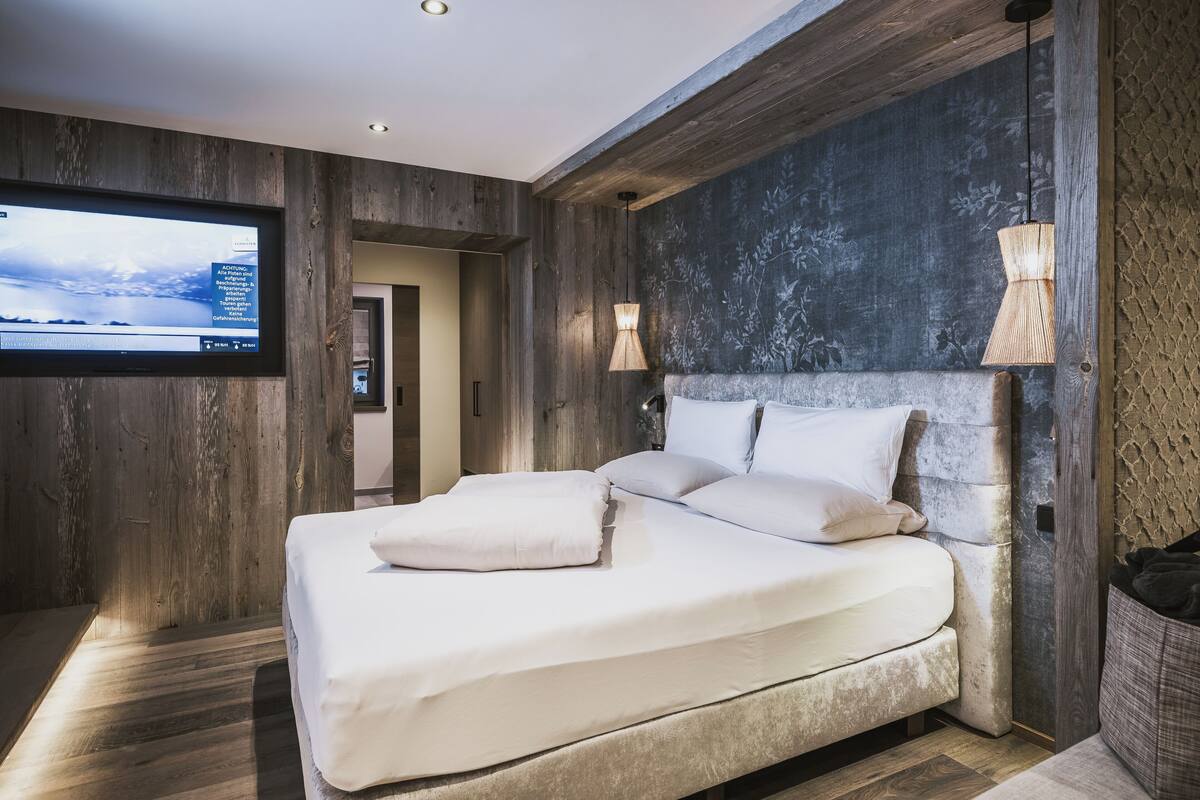 Ein modernes Schlafzimmer mit einem großen Bett, Holzwänden, einem an der Wand montierten Fernseher und einer einzigartigen, strukturierten Wand hinter dem Bett.