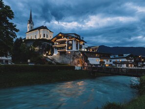 Un bâtiment historique doté d’un clocher d’église, d’une grande formation rocheuse et d’une rivière au premier plan.