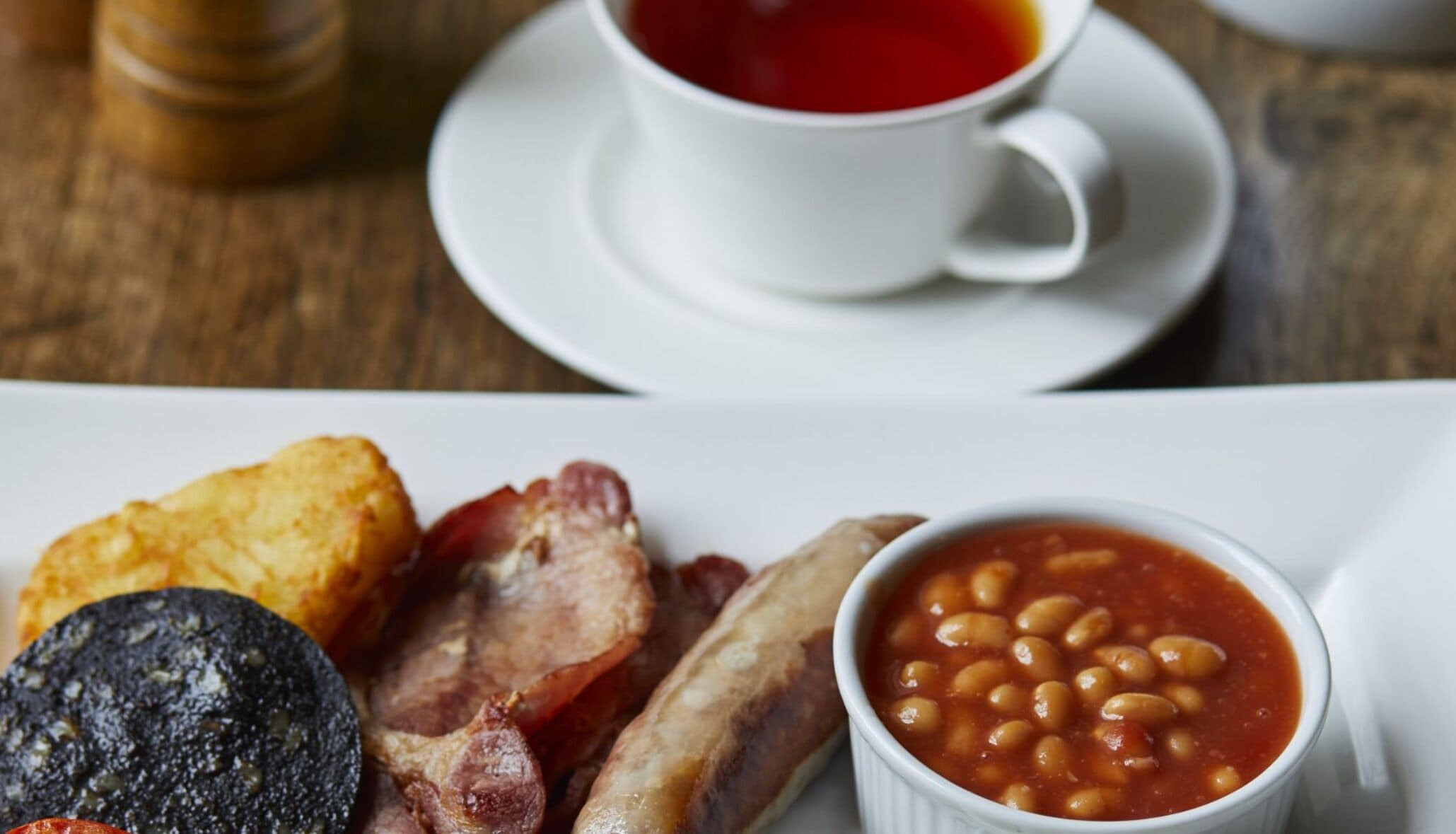 A breakfast plate with bacon, sausages, black pudding, and baked beans.