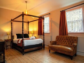 A four-poster bed with a wooden frame, a tufted leather armchair, and a nightstand with a lamp.