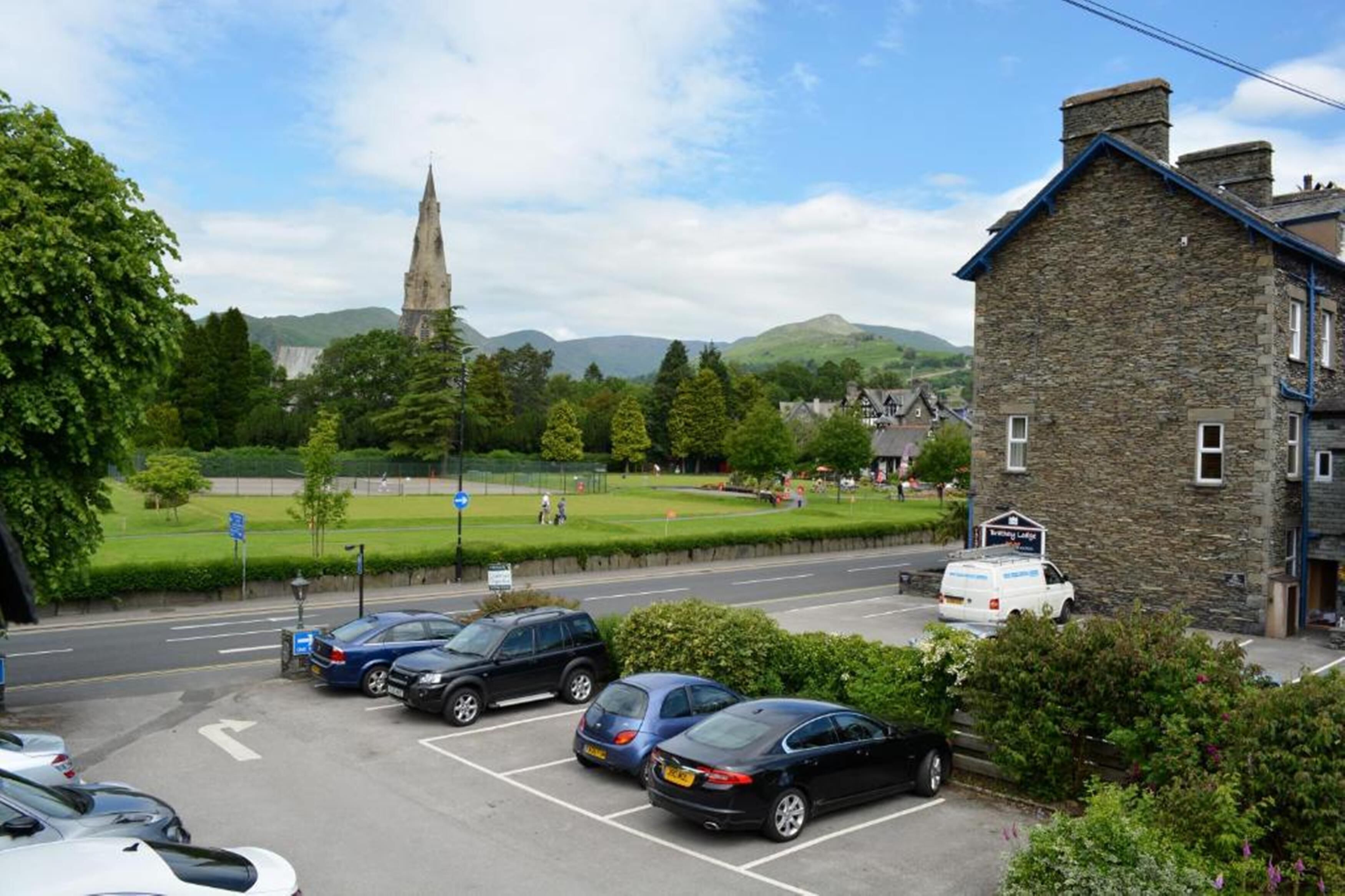 A parking lot with several cars, a stone building, and a church in the background.