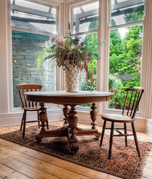 A dining table with a white vase of flowers, two wooden chairs, and a patterned rug.