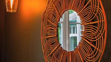 A wall-mounted circular mirror with a woven frame, a hanging light fixture, and a reflection of a building.