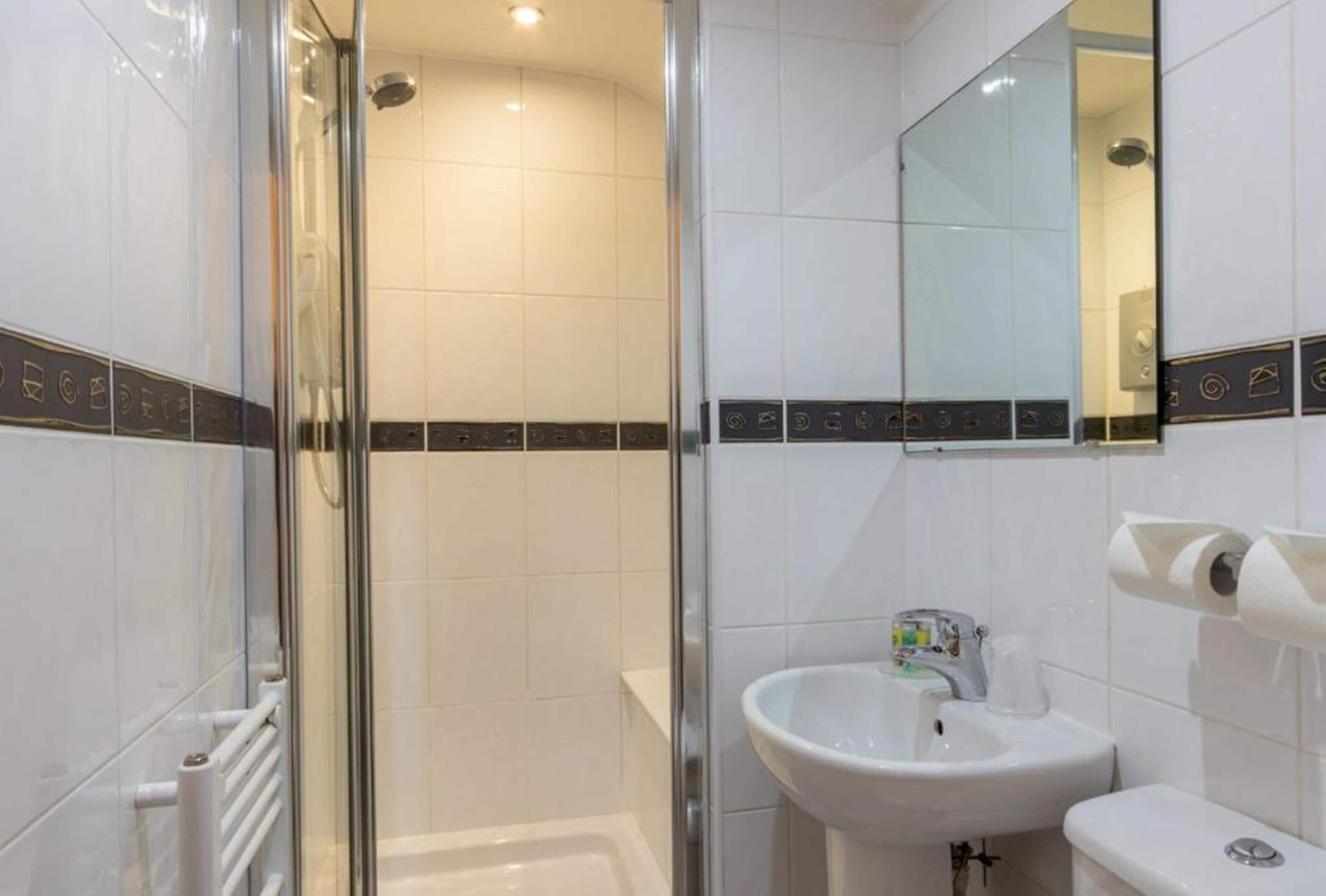 Un baño moderno con cabina de ducha de vidrio, un lavamanos blanco y un inodoro.