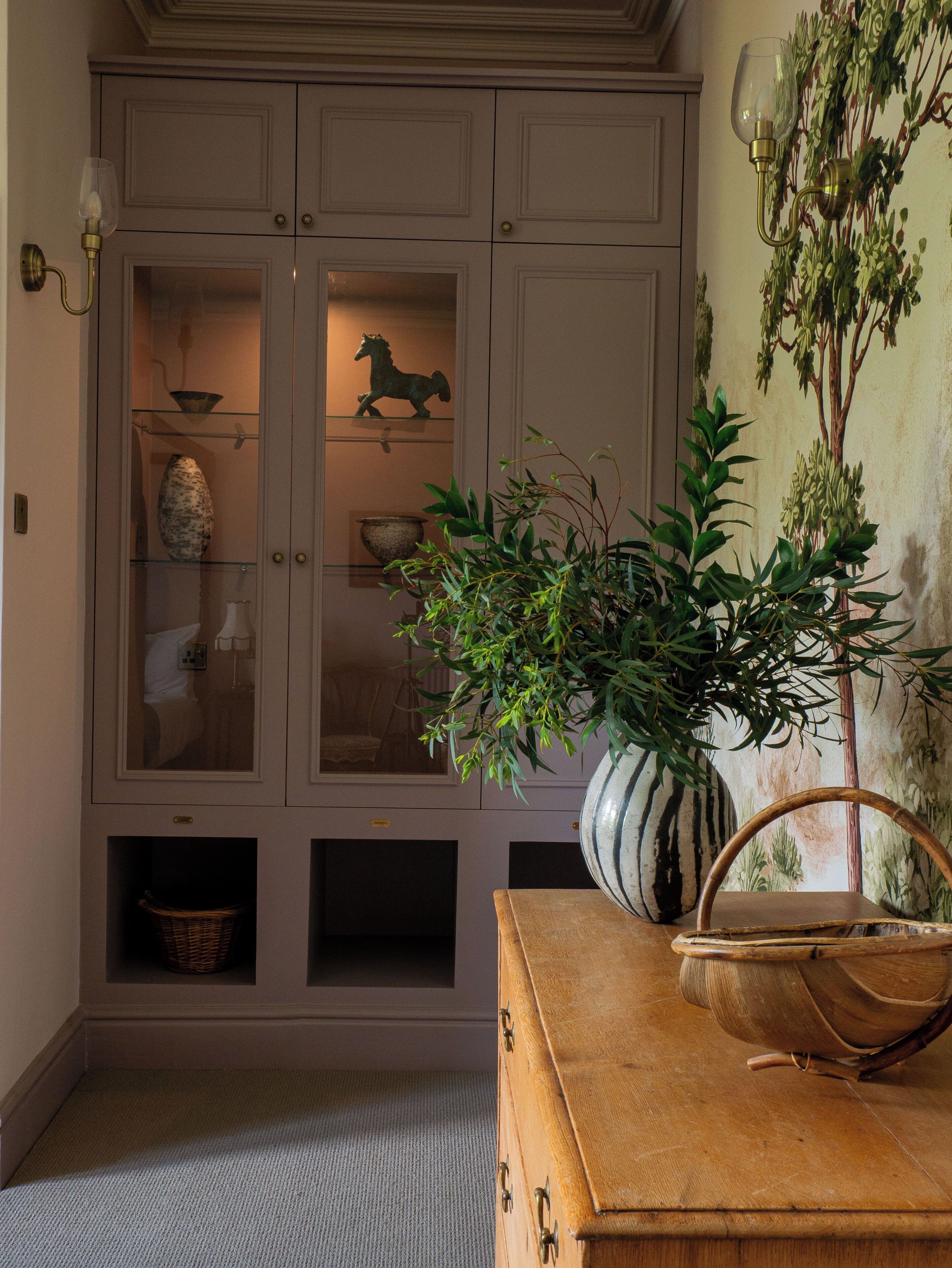 A room with a cabinet containing decorative items, a potted plant, and a wooden chest.