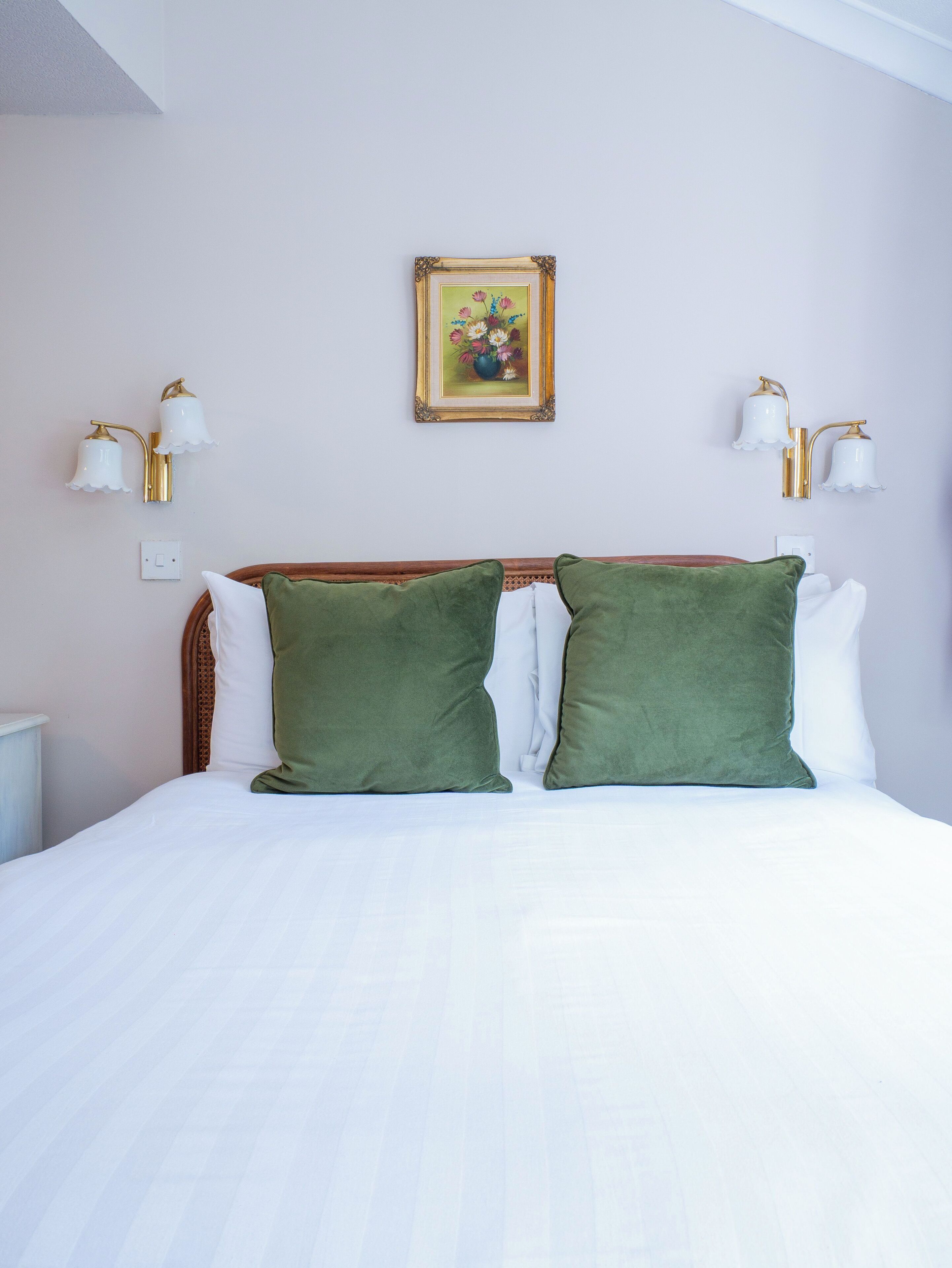 A bed with two green pillows, a white comforter, and a wall-mounted picture frame.