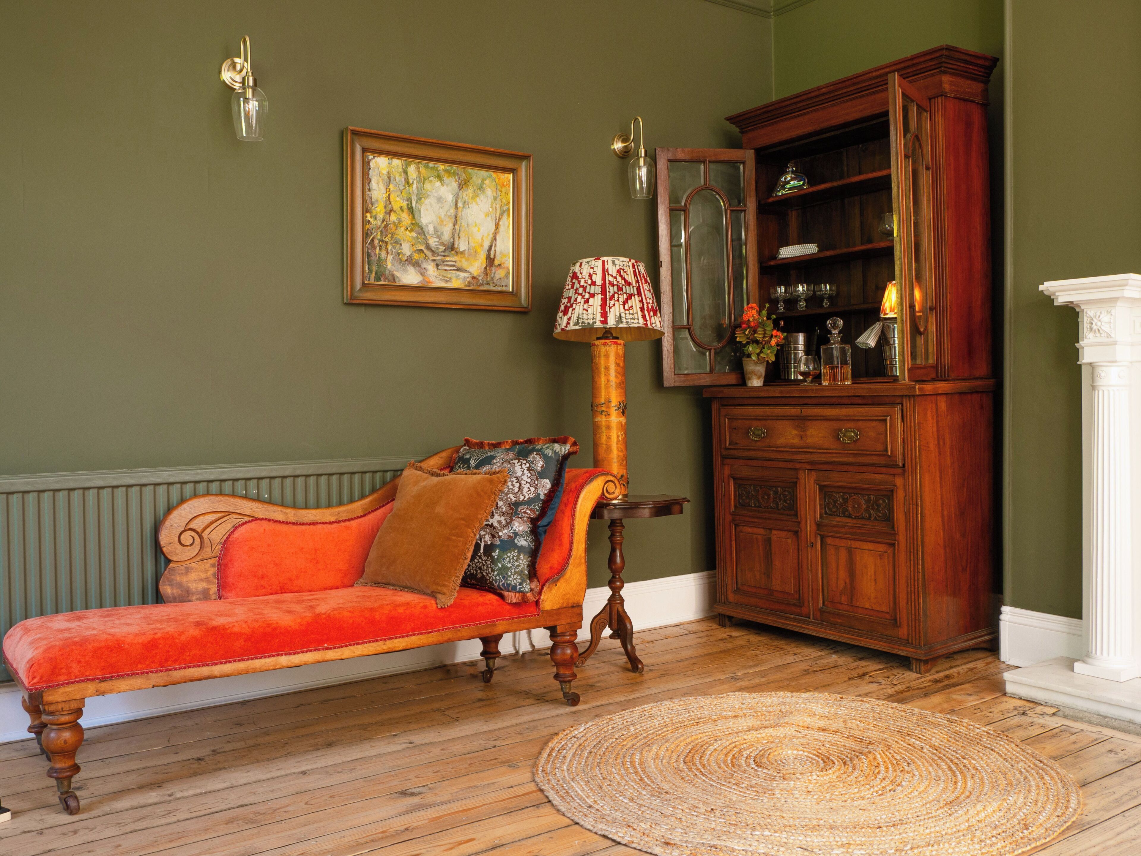 A room with a red sofa, a wooden cabinet, a lamp, and a painting on the wall.