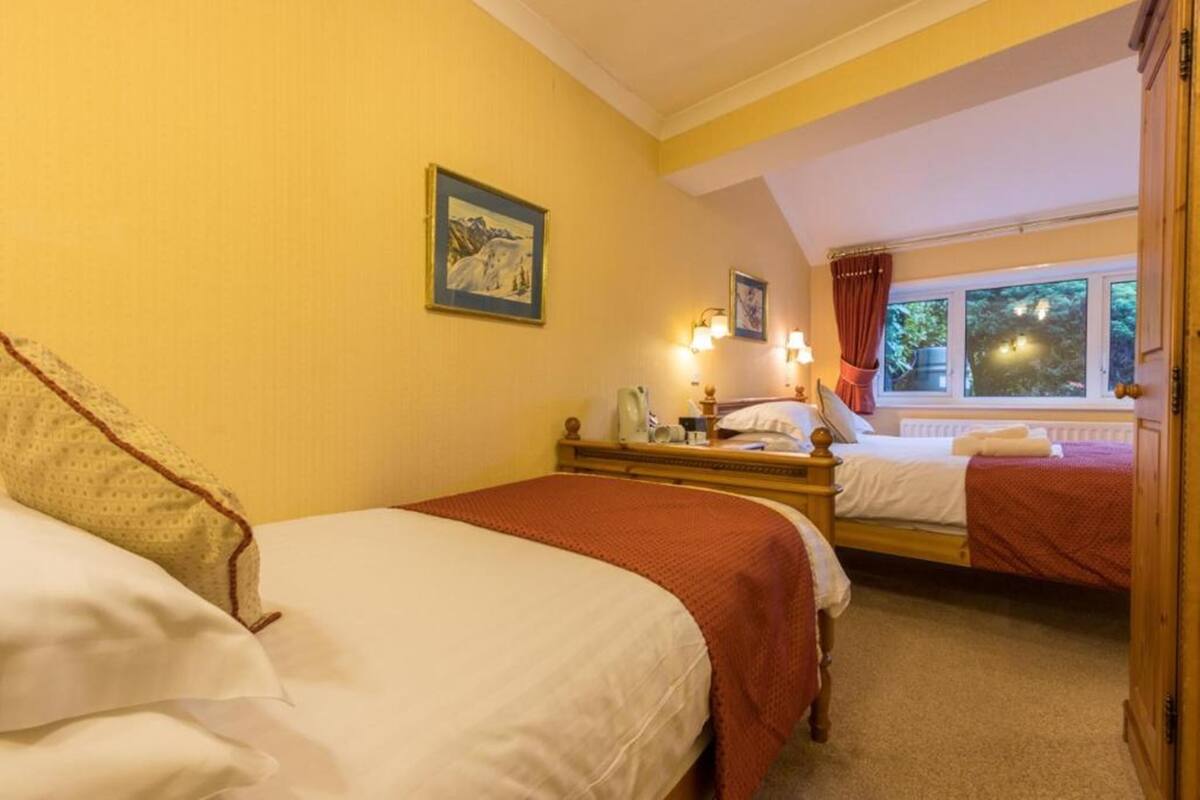 A hotel room with two beds, a window with curtains, and a painting on the wall.
