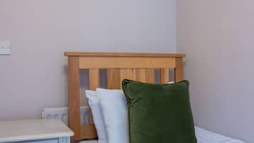 Un dormitorio con cabecera de madera, una mesita de noche blanca, un almohadón verde y una lámpara de pared.