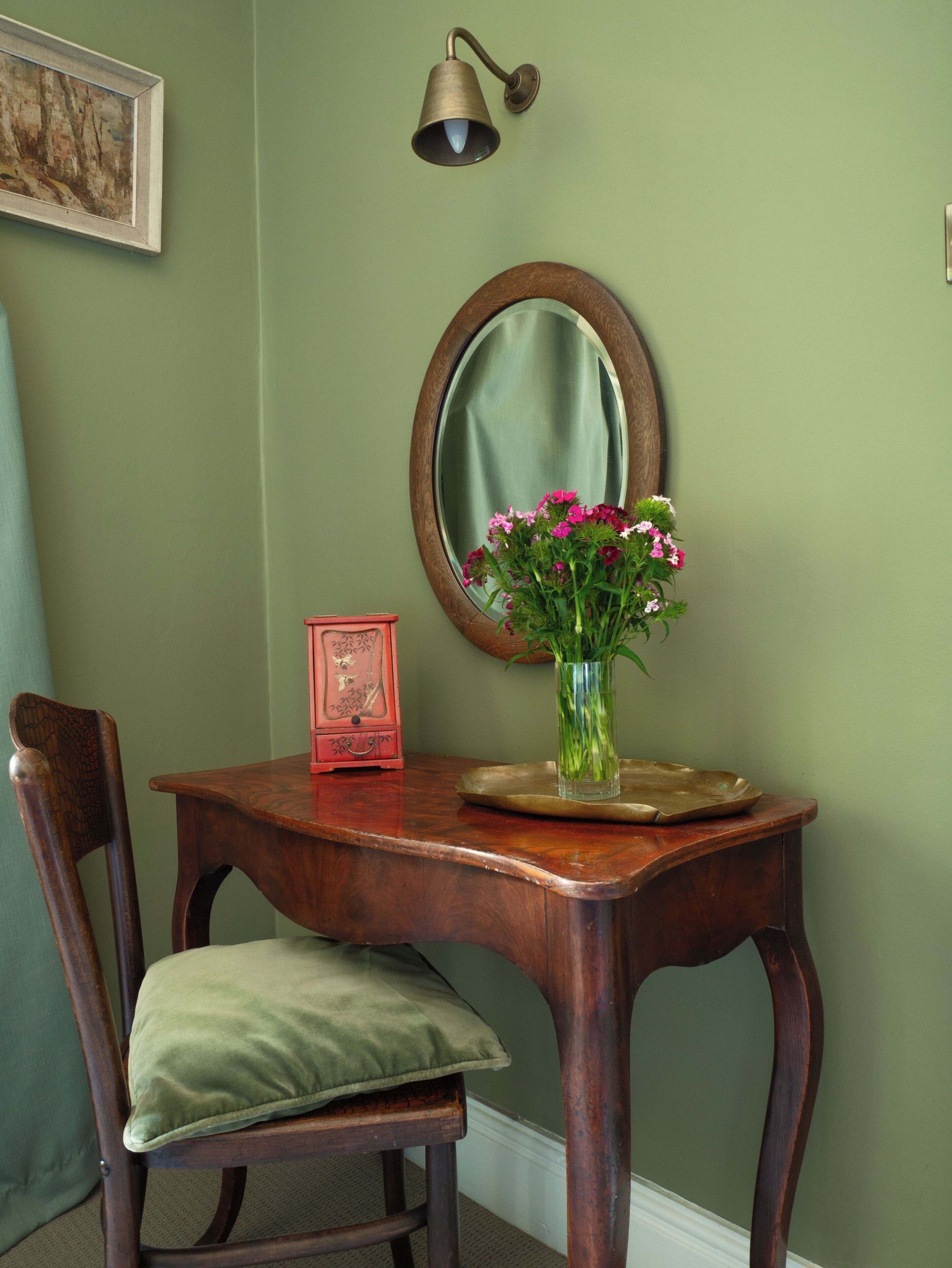 Une table en bois ornée d’un vase de fleurs, d’un miroir et d’un luminaire fixé au mur.