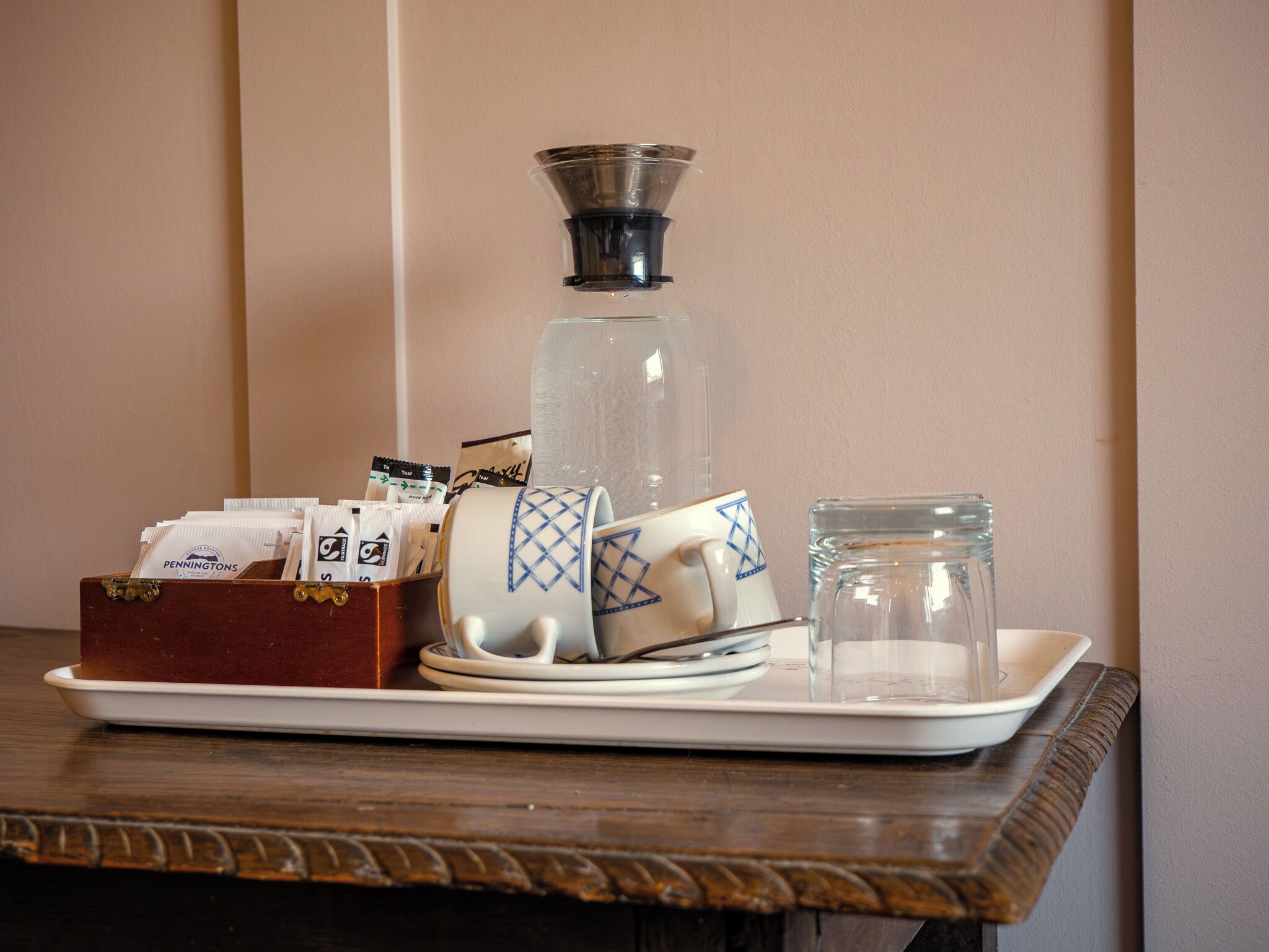 A tray with a coffee maker, a glass jar, a mug, and a box of tea bags.