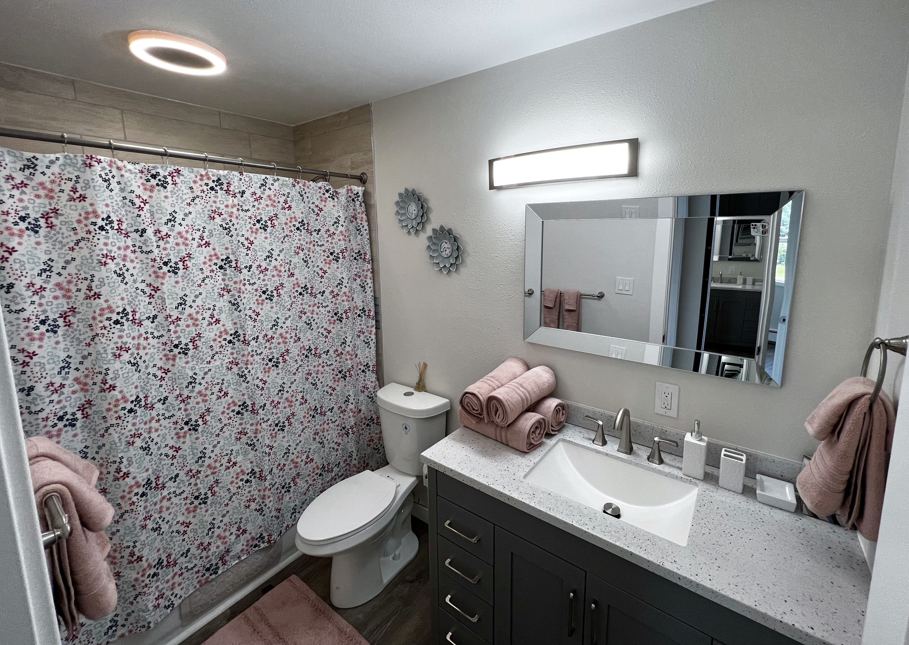 A bathroom with a shower curtain, toilet, sink, and mirror.