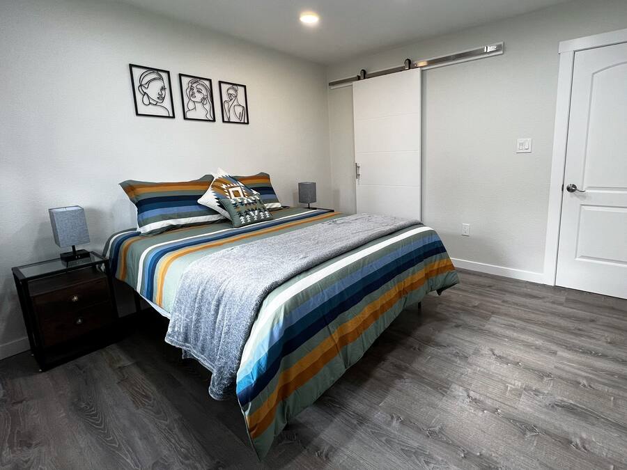 A bedroom with a bed, nightstands, a dresser, a sliding door, and three framed artworks on the wall.