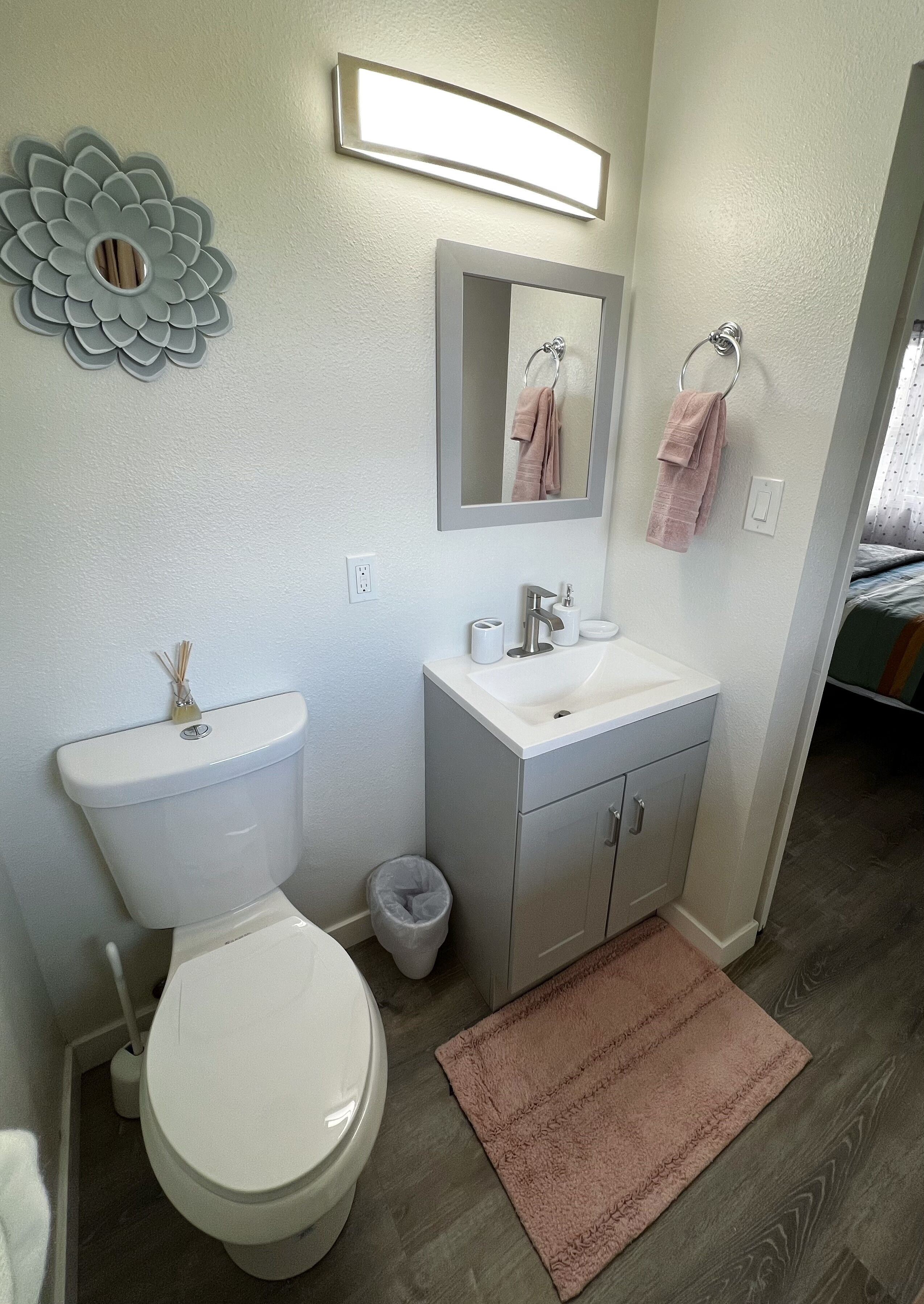 A bathroom with a toilet, sink, mirror, and decorative wall piece.