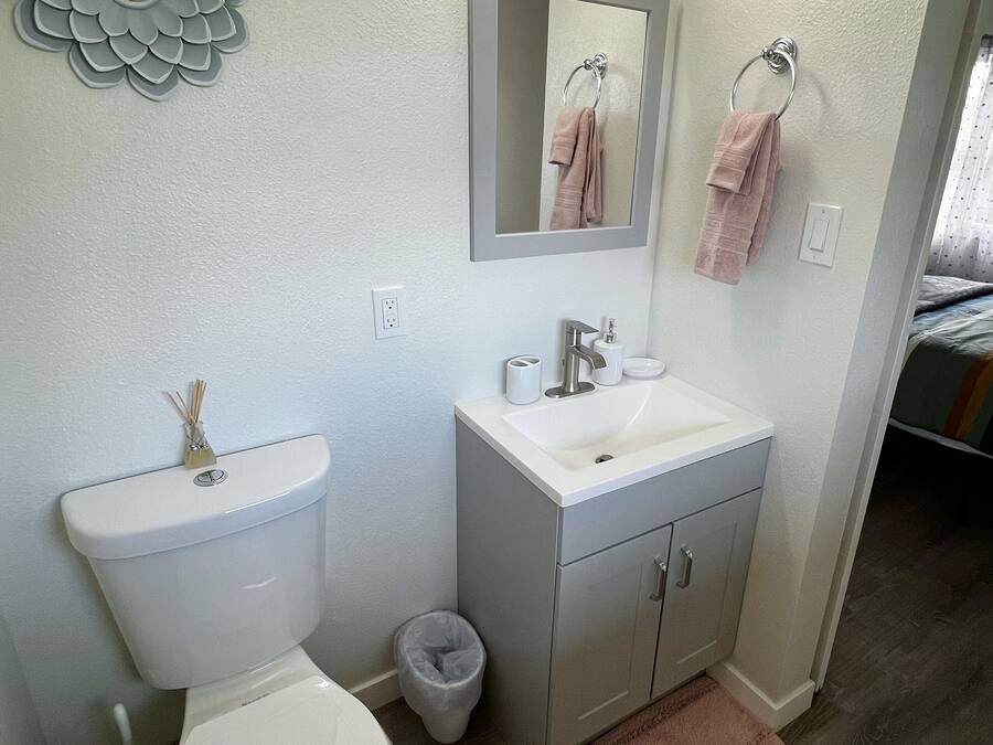 A bathroom with a toilet, sink, mirror, and decorative wall piece.