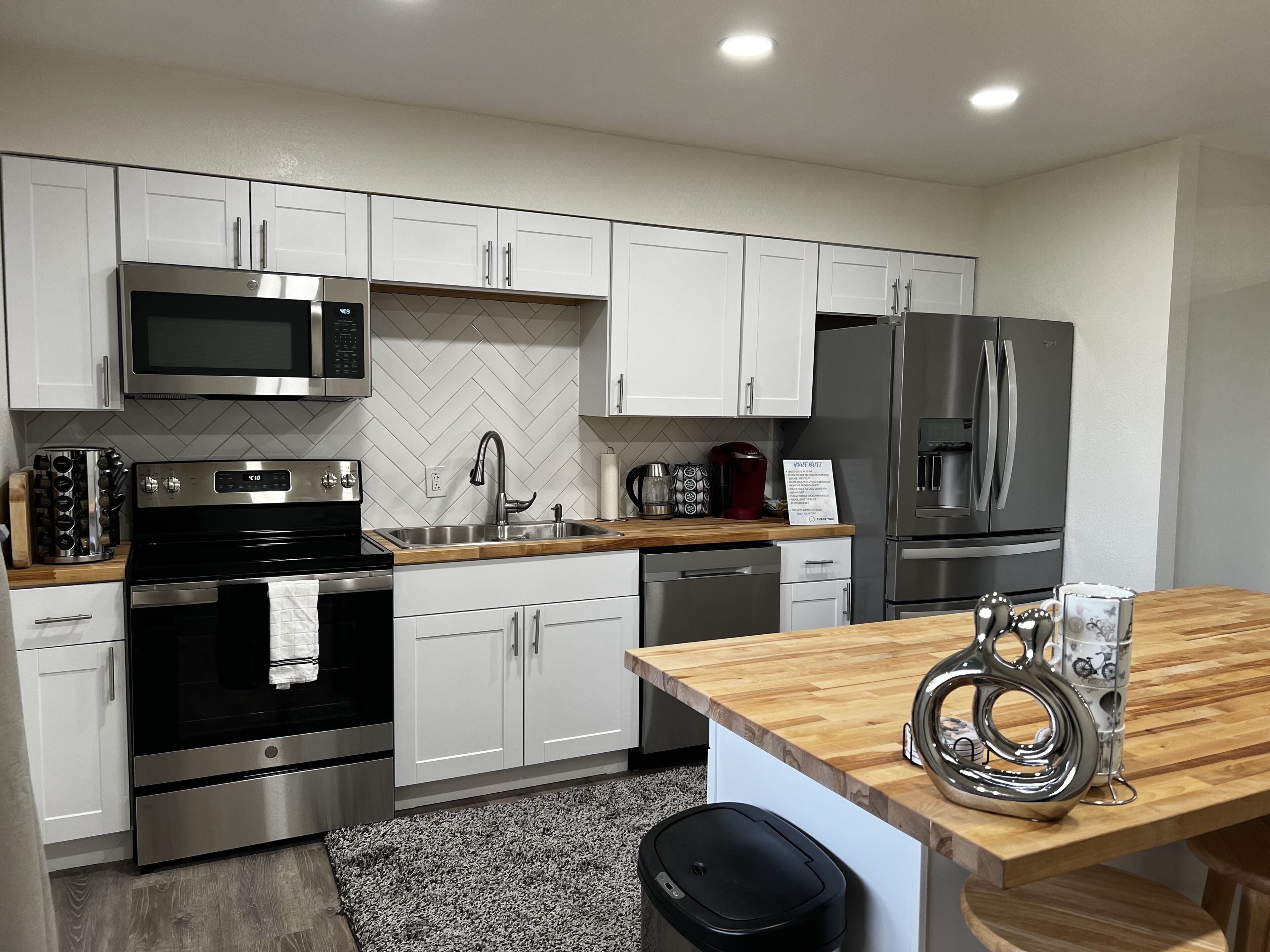 A modern kitchen with white cabinets, stainless steel appliances, and a wooden countertop.