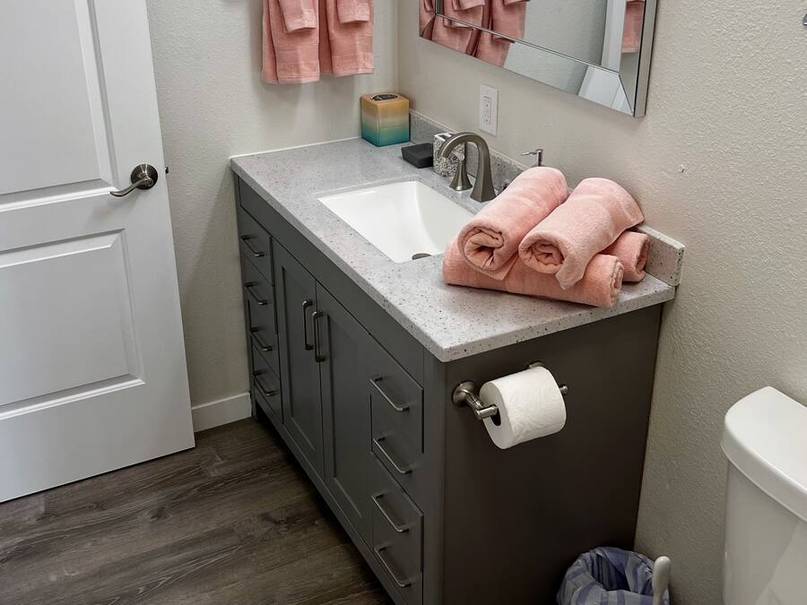 A bathroom with a white toilet, a sink with a mirror above it, and two pink towels hanging on a towel rack.