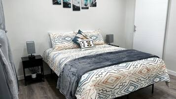 A bedroom with a bed, patterned bedding, a nightstand with a lamp, and wall art.