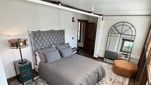 Un dormitorio con una cama grande, una mesita de noche, una silla y una ventana con vistas.