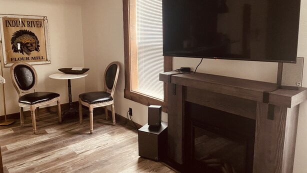 A room with a fireplace, a television mounted above it, a small table with a chair, and a poster on the wall. - New Listing! In Downtown Red Lodge. Excellent Location! (Red Lodge)