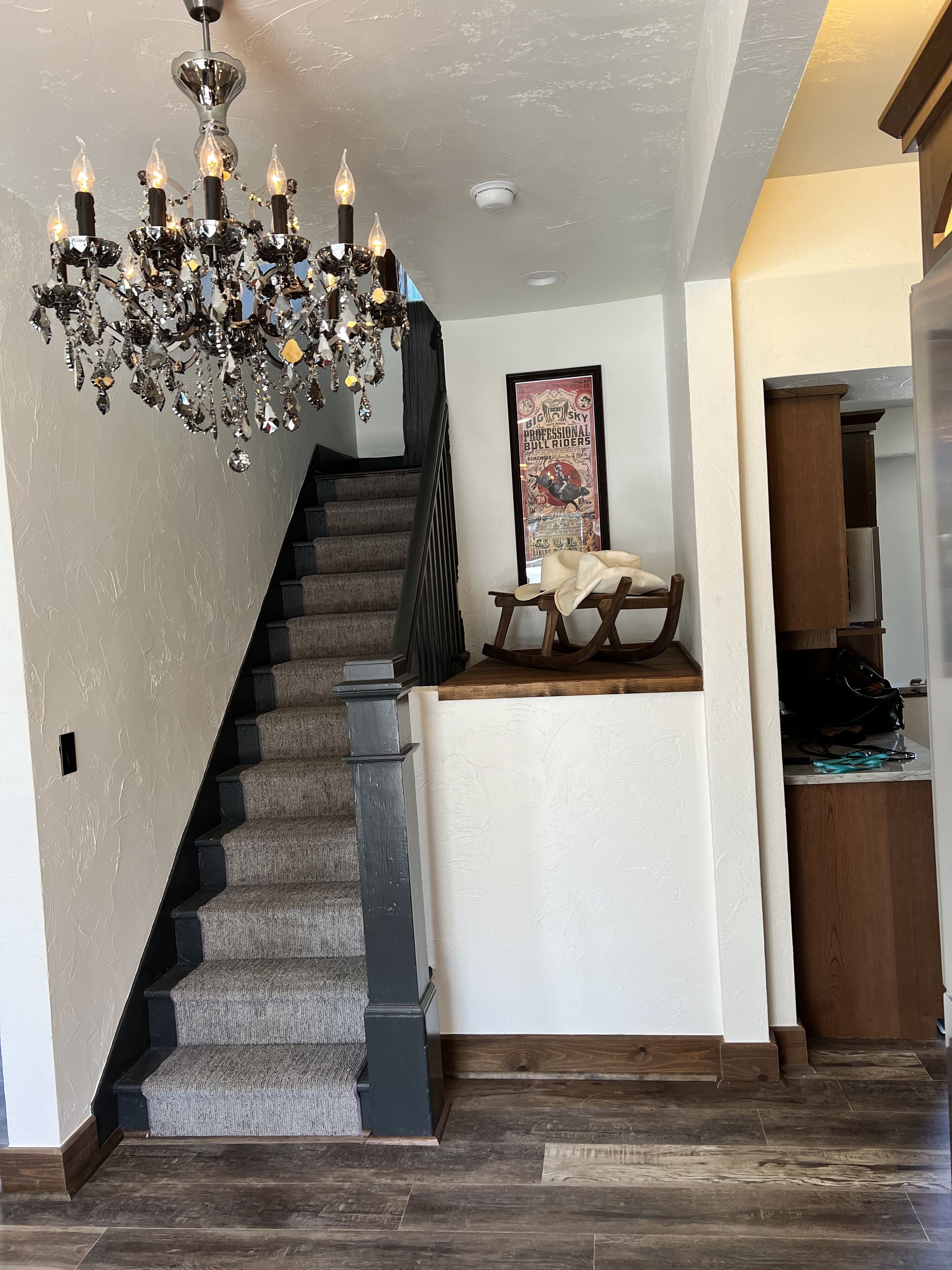 A staircase with a dark carpet and black balusters, leading to a landing with a framed poster and a small table.