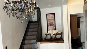 Una escalera con alfombra oscura y barandilla negra, que conduce a un rellano con un cartel enmarco y una pequeña mesa.
