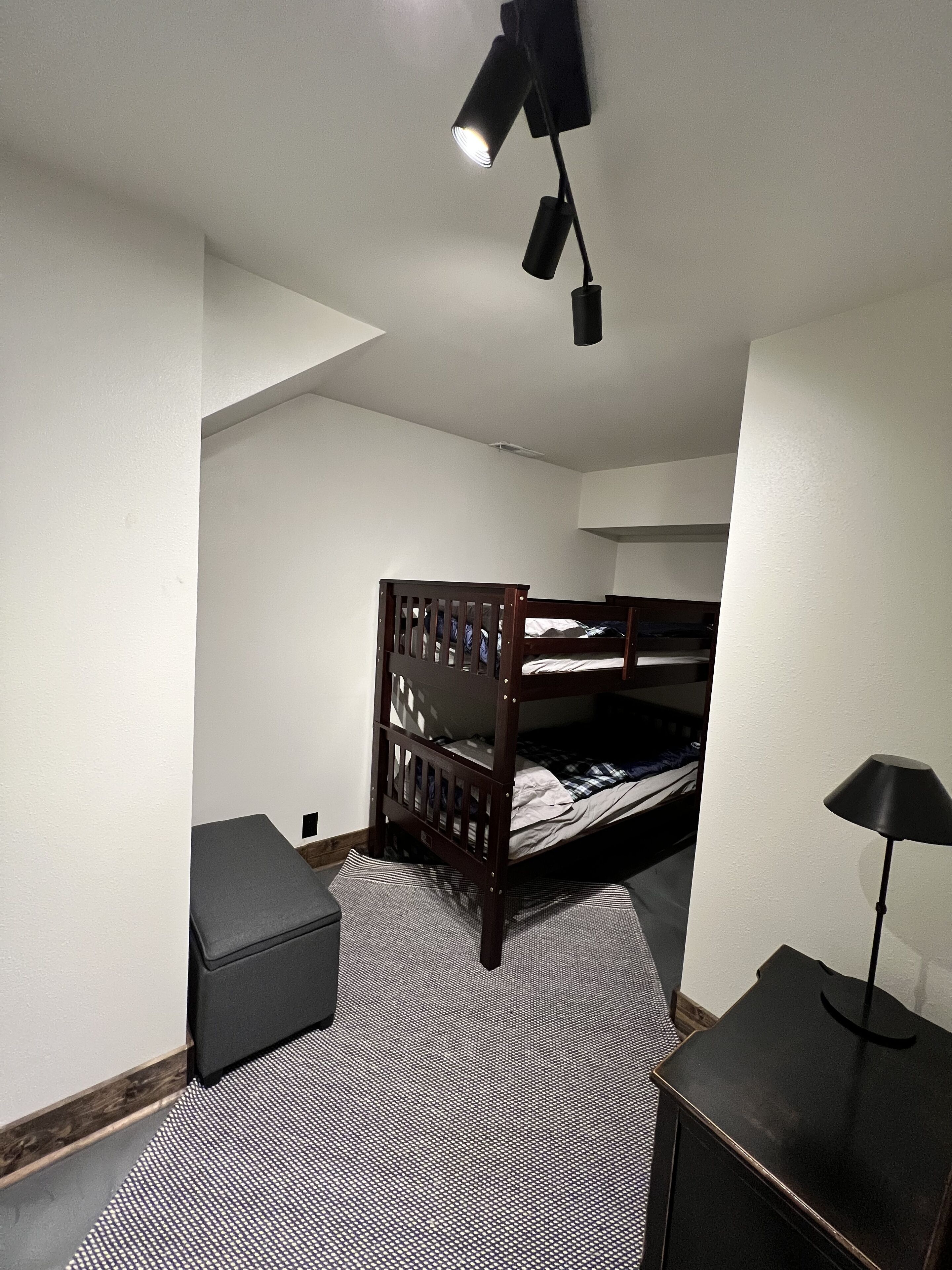 A room with a bunk bed, a desk with a lamp, and a patterned rug.