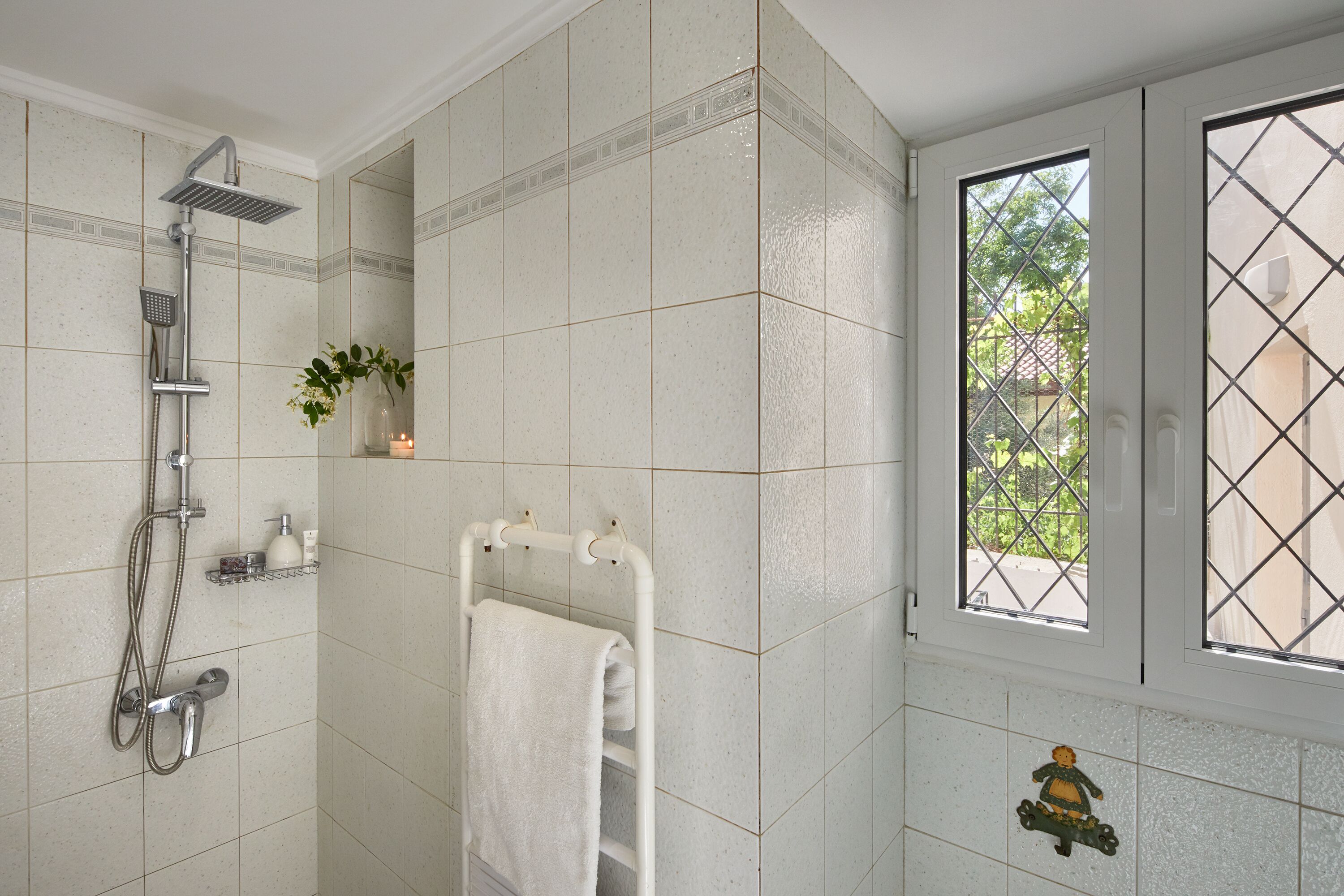 A bathroom with a shower, a towel rack, and a window with a view of greenery.