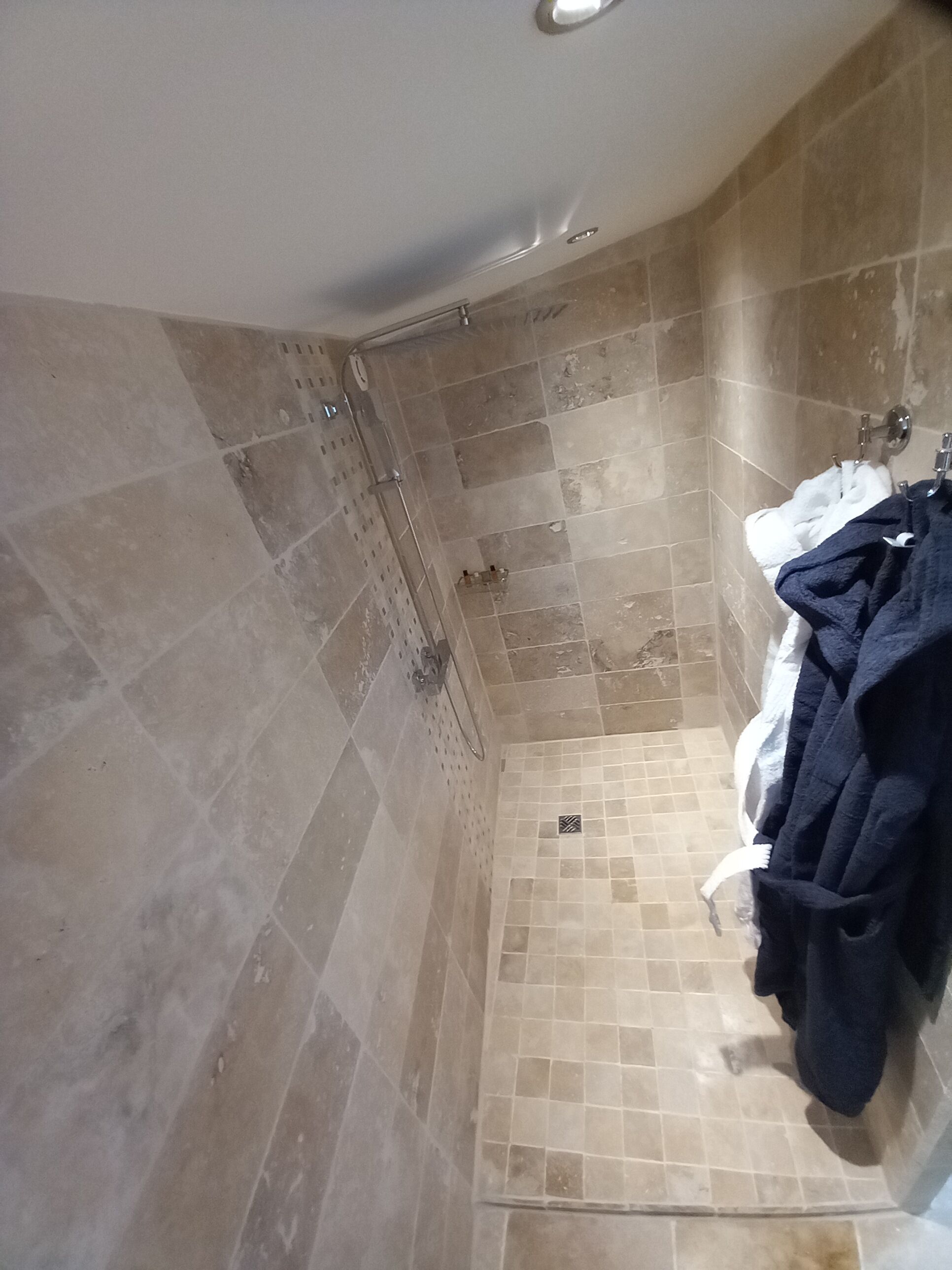 A bathroom with beige tiles, a shower, a sink, and a towel rack with towels.