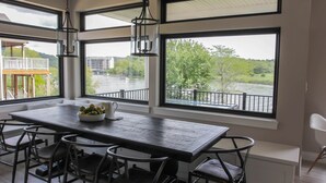 A dining area with a large table, chairs, and a view of a river through large windows.