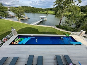 A swimming pool with lounge chairs and inflatable toys, overlooking a lake with boats and a golf course.