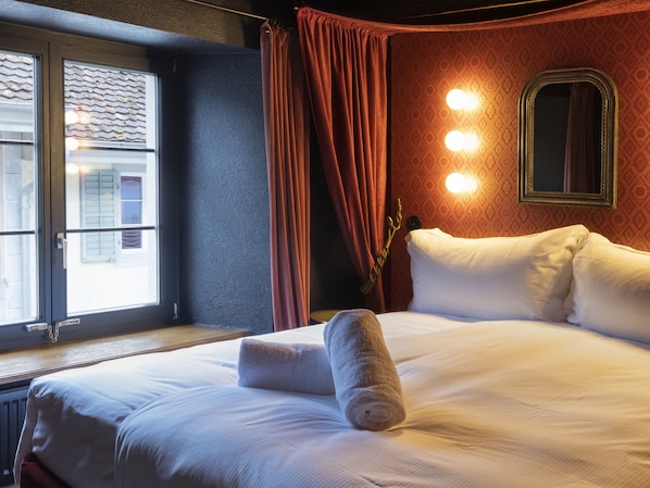 Habitación de hotel con una cama grande, una ventana con cortinas, un espejo y luces fijadas a la pared.