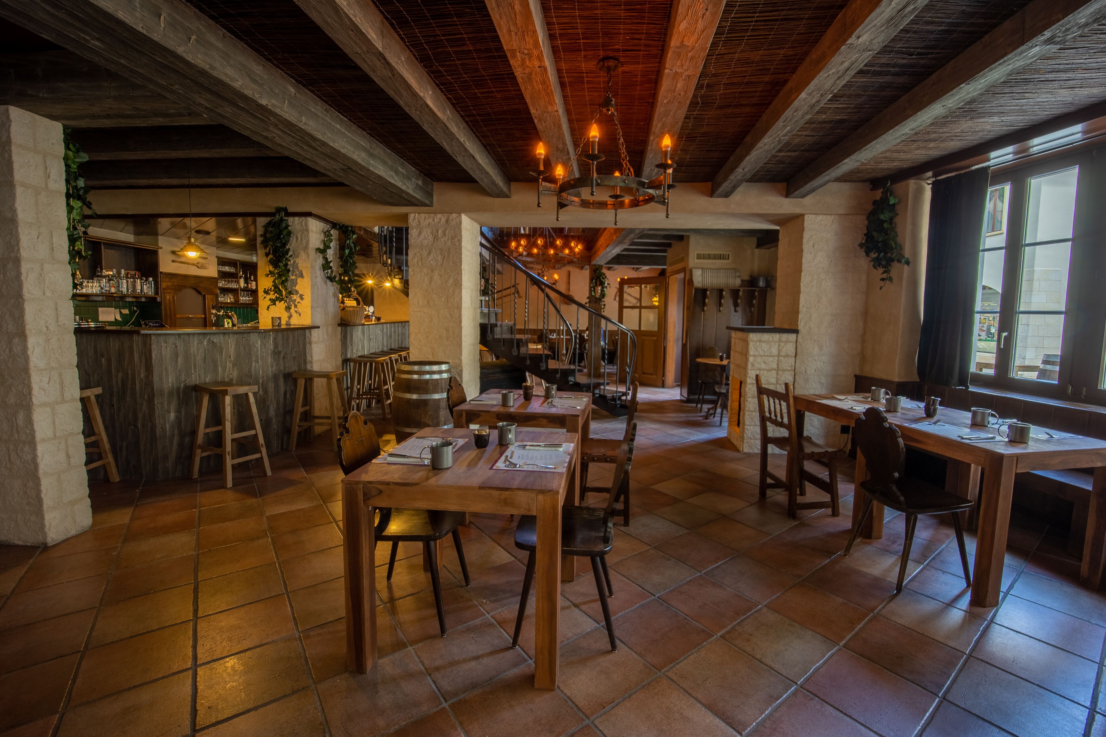 Ein Restaurant mit Holztischen und -stühlen, einem Barbereich und einer Treppe, die zu einer oberen Ebene führt.