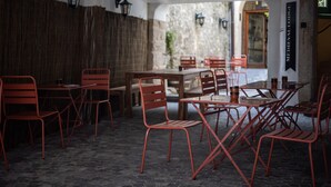 Un comedor interior con sillas y mesas de metal rojo, paredes de piedra y faroles colgantes.