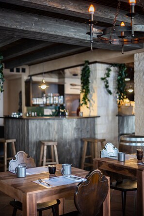 Interior de restaurante con mesas de madera, sillas de metal y lámparas colgantes.