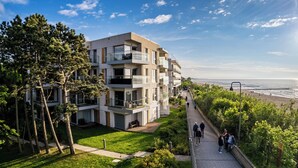 A modern multi-story residential building with balconies, a pathway leading to a beach, and lush greenery. - Apartamenty Sun&Snow Przy Plaży (Mielno)